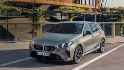 Ein silberner BMW 1er mit Schrägheck ist auf einer Straße vor einem modernen, begrünten Gebäude geparkt.