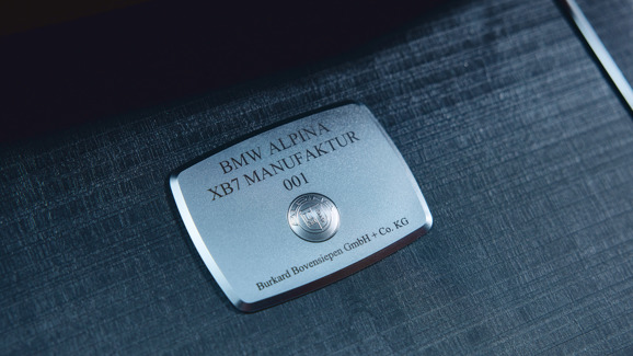 „Detailaufnahme einer silbernen BMW ALPINA Manufakturplakette mit der Gravur 'BMW ALPINA XB7 MANUFAKTUR 001' und dem ALPINA-Logo, montiert auf einer edlen Holz- oder Metalloberfläche im Innenraum.“