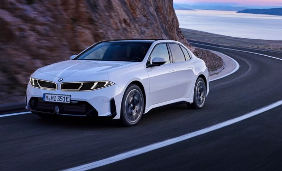 Eine weiße BMW-Limousine fährt auf einer kurvenreichen Küstenstraße, auf der einen Seite ragen Klippen empor, und im Hintergrund erstreckt sich das Meer.