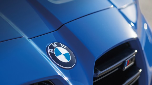 Nahaufnahme der Motorhaube eines blauen BMW, auf der das BMW-Logo und ein Teil des Kühlergrills zu sehen sind.