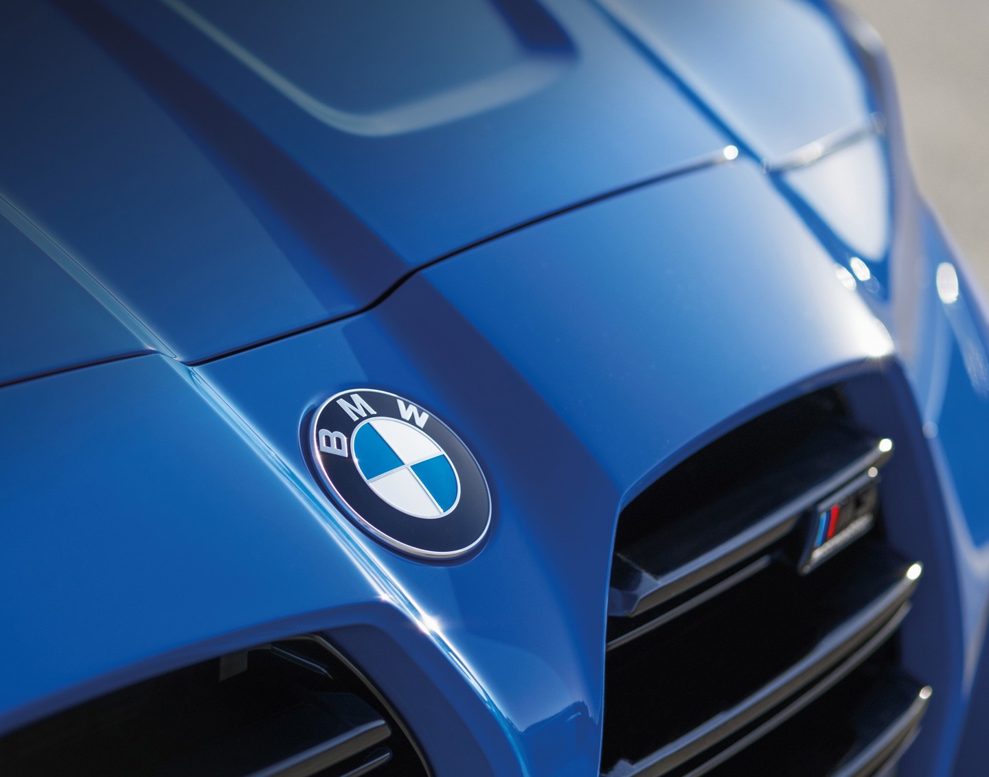 Nahaufnahme der Motorhaube eines blauen BMW, auf der das BMW-Logo und ein Teil des Kühlergrills zu sehen sind.