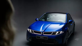 Eine blaue BMW-Limousine wird unter Studiobeleuchtung gezeigt, von vorne gesehen, mit einer Person im Vordergrund.
