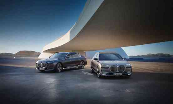 „Zwei BMW Luxuslimousinen der 7er-Reihe stehen nebeneinander auf einem futuristischen Platz unter einer modernen, geschwungenen Architektur. Im Hintergrund sind Berge und ein weiter Horizont zu sehen.“