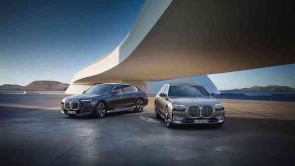 „Zwei BMW Luxuslimousinen der 7er-Reihe stehen nebeneinander auf einem futuristischen Platz unter einer modernen, geschwungenen Architektur. Im Hintergrund sind Berge und ein weiter Horizont zu sehen.“