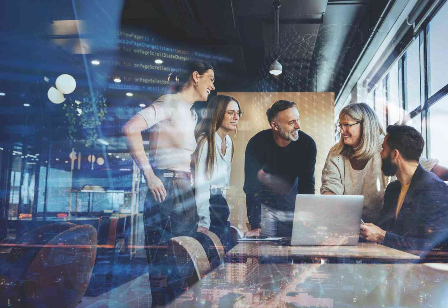 „Ein gemischtes Team aus fünf Personen steht um einen Tisch in einem modernen Büro und arbeitet gemeinsam an einem Laptop. Überlagert ist das Bild mit digitalen Codezeilen, Netzwerkgrafiken und Stadtlichtern – Symbol für Digitalisierung, Teamwork und Innovation.“