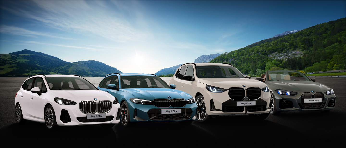Vier BMW-Fahrzeuge stehen im Freien in einer Reihe, im Hintergrund sind unter klarem Himmel Berge und Grünflächen zu sehen.