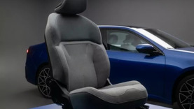 In einem modernen, minimalistischen Ausstellungsraum steht ein Autositz auf einem blauen Sockel vor einem blauen Auto.