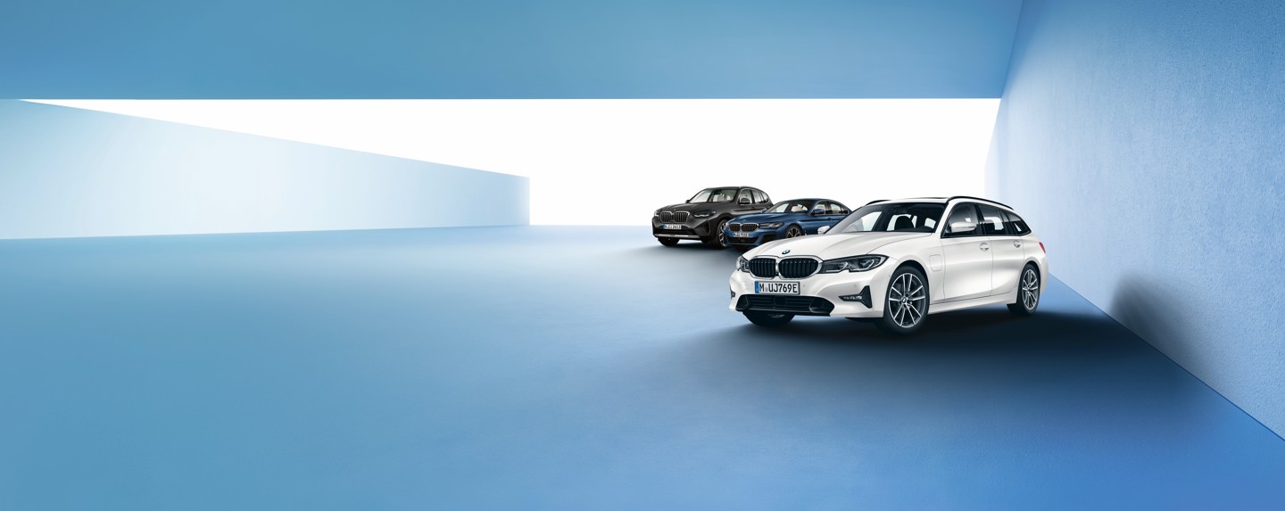 Drei BMW-Fahrzeuge, darunter ein weißer Kombi ganz vorne, stehen in einer minimalistisch gestalteten blau-weißen Innenkulisse.