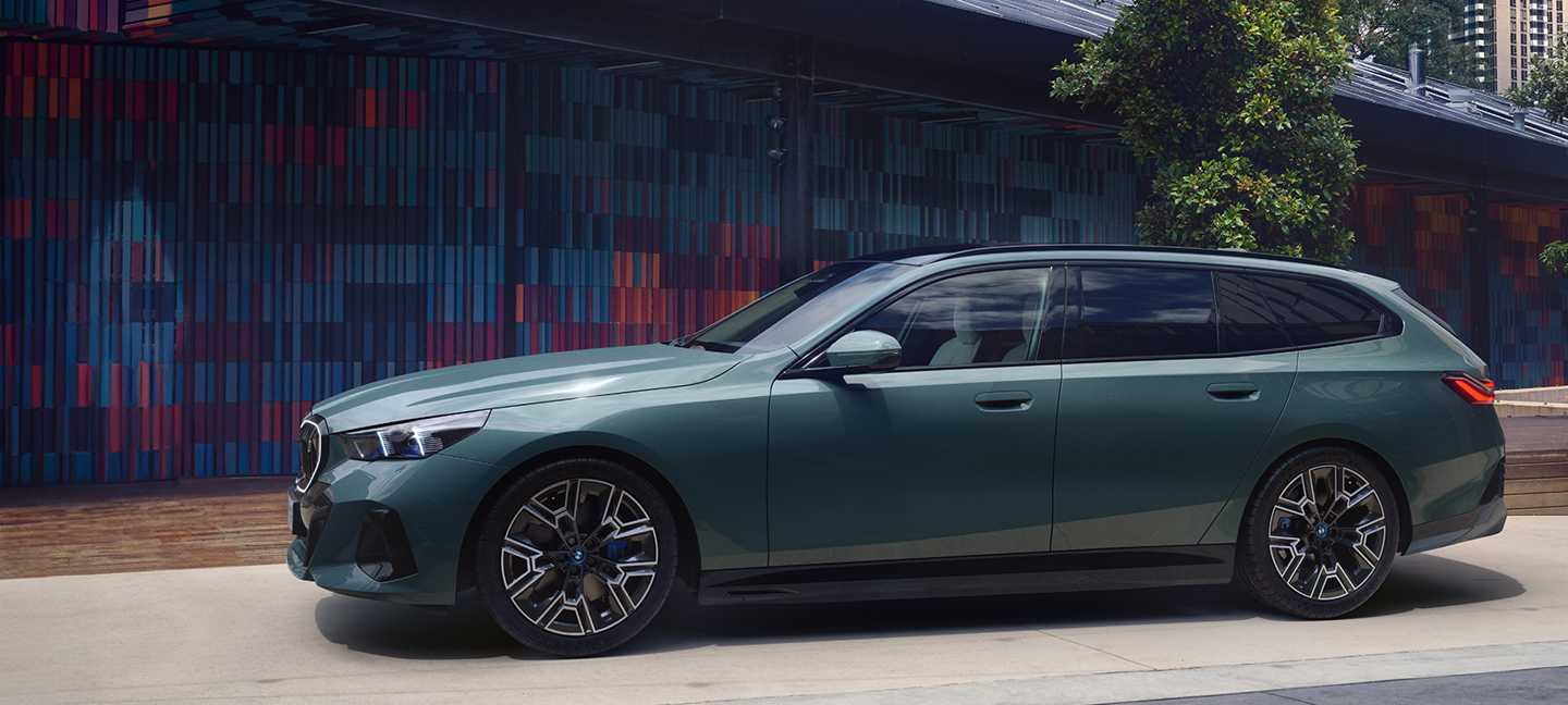 Ein grüner BMW 5er Touring steht seitlich vor einer modernen Fassade mit bunten Wandfliesen. Der Premium-Kombi wirkt elegant und sportlich.
