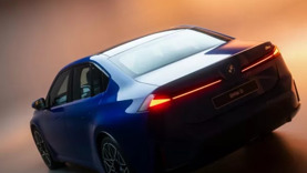 Ein blauer BMW i3 ist schräg von hinten zu sehen, mit leuchtenden Rückleuchten und einem orange-weißen Hintergrund mit Farbverlauf.
