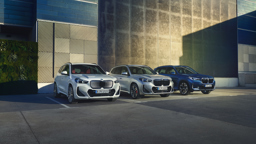 Drei BMW X1 Modelle nebeneinander vor einer modernen Gebäudefassade: links ein weißer BMW X1 xDrive25e Plug-in-Hybrid, in der Mitte ein silberner BMW X1 mit sportlicher M-Ausstattung und rechts ein blauer vollelektrischer BMW iX1. Im Hintergrund ein blauer Kreis mit dem Schriftzug „Alle Angebote inkl. Wartung und Reparatur.“
