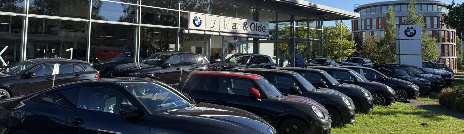 BMW und MINI Fahrzeuge vor dem May & Olde Autohaus in Ahrensburg bei sonnigem Wetter, mit Glasfassade und BMW Logo-Stele