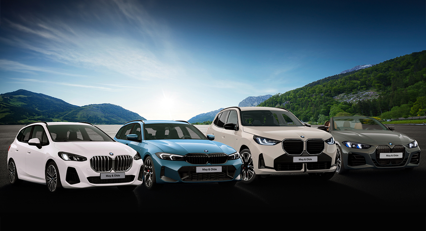 Vier BMW-Fahrzeuge stehen nebeneinander im Freien, vor der Kulisse von Bergen und einem See unter klarem Himmel.