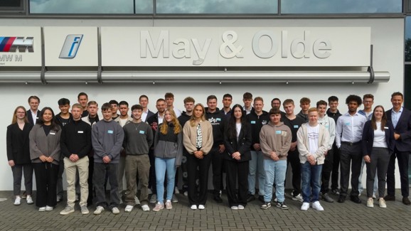 Gruppenfoto der neuen Auszubildenden 2025 von May & Olde vor dem Autohaus mit großem Firmenlogo; junge Menschen stehen in mehreren Reihen und blicken lächelnd in die Kamera – gemeinsamer Start in das Berufsleben bei BMW und MINI.