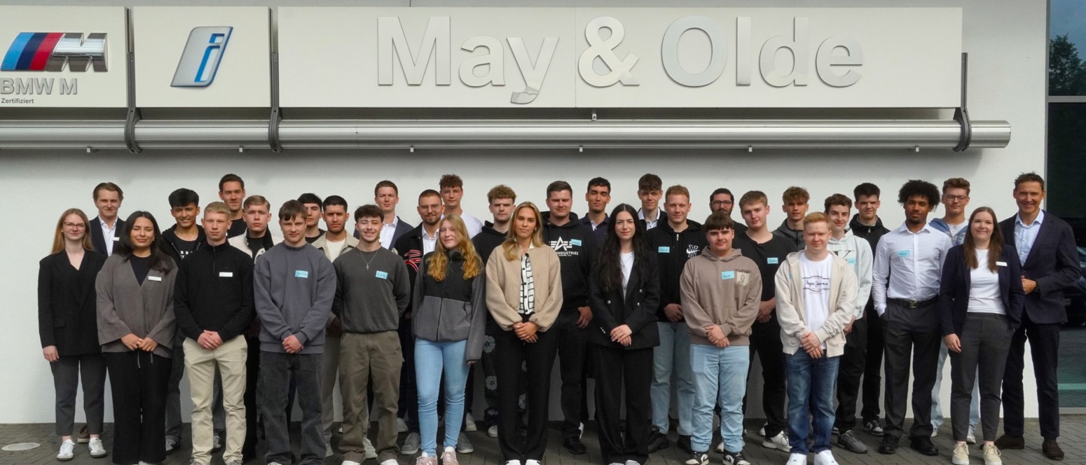 Gruppenfoto der neuen Auszubildenden 2025 von May & Olde vor dem Autohaus mit großem Firmenlogo; junge Menschen stehen in mehreren Reihen und blicken lächelnd in die Kamera – gemeinsamer Start in das Berufsleben bei BMW und MINI.