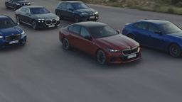 Mehrere neue BMW Modelle fahren nebeneinander auf einer Straße, darunter Limousinen und SUVs in verschiedenen Farben. 