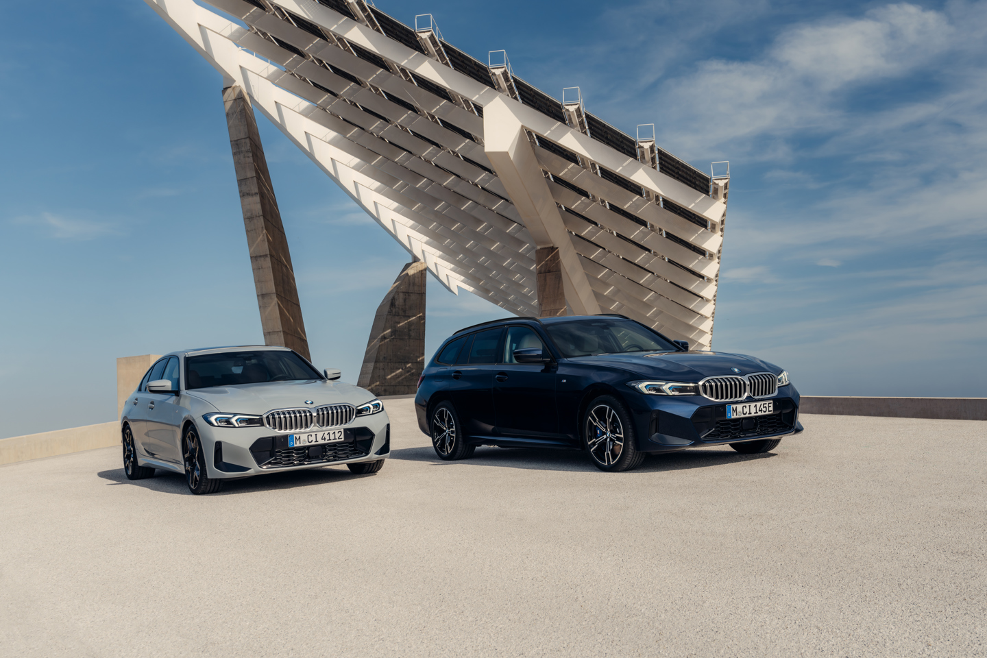 BMW 3er Limousine in Silber und BMW 3er Touring in Dunkelblau vor moderner Architektur mit Solarpanel-Dach, präsentiert bei sonnigem Wetter für eine elegante und dynamische Inszenierung.   