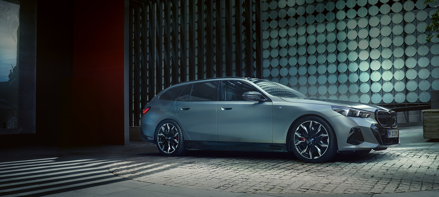 Ein grüner BMW 5er Touring steht seitlich vor einer modernen Fassade mit bunten Wandfliesen. Der Premium-Kombi wirkt elegant und sportlich.