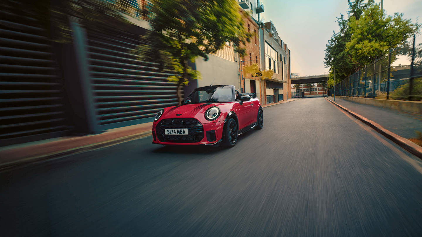 Ein rotes Cabrio fährt eine leere, von Gebäuden und Bäumen gesäumte Stadtstraße entlang.
