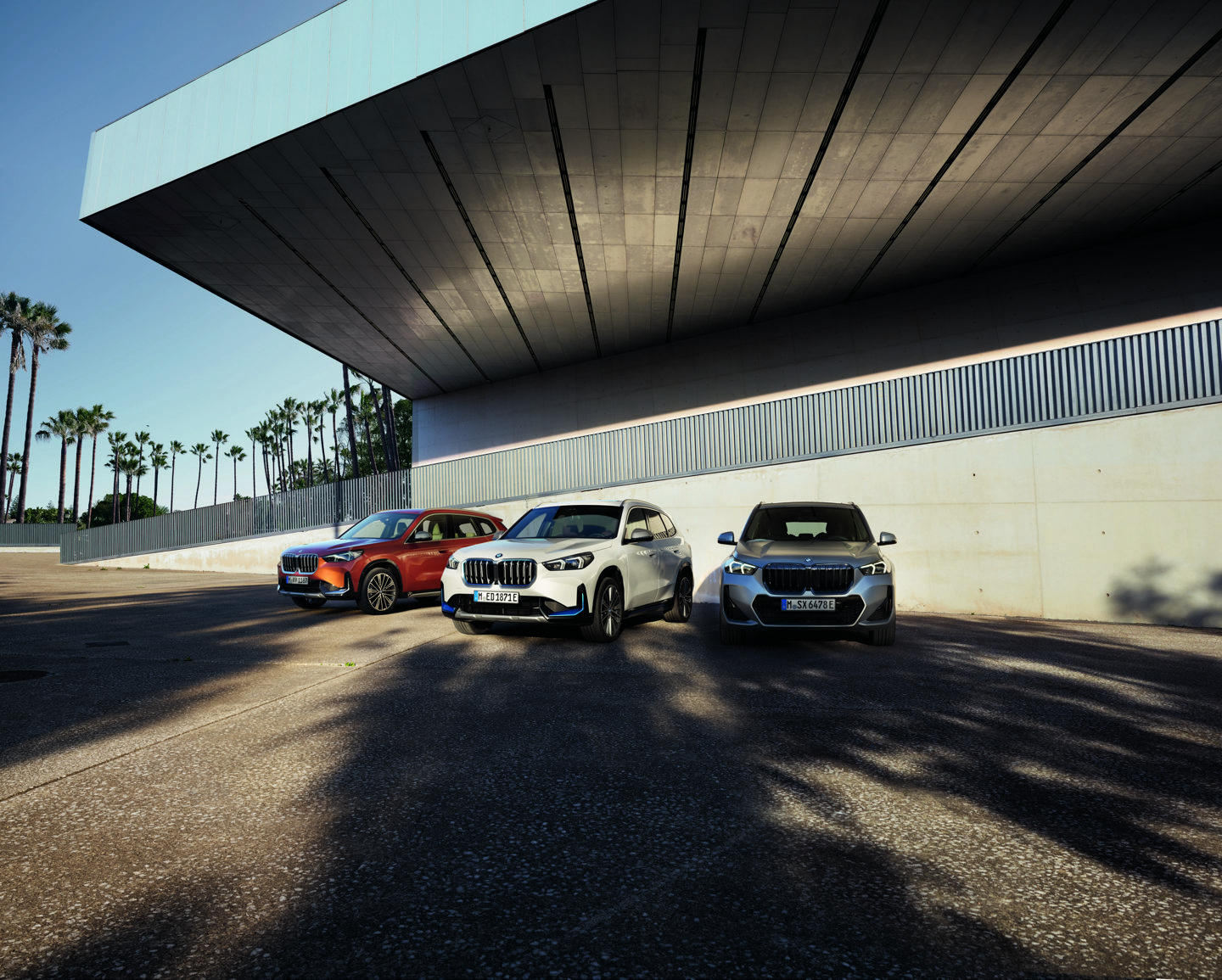 Drei BMW X1 Modelle stehen nebeneinander vor moderner Architektur – Sinnbild für die Power of Choice: Benzin, Plug-in-Hybrid und vollelektrisch. Entspannte Mobilität und individuelle Freiheit mit Relax. We. Care. bei May & Olde.