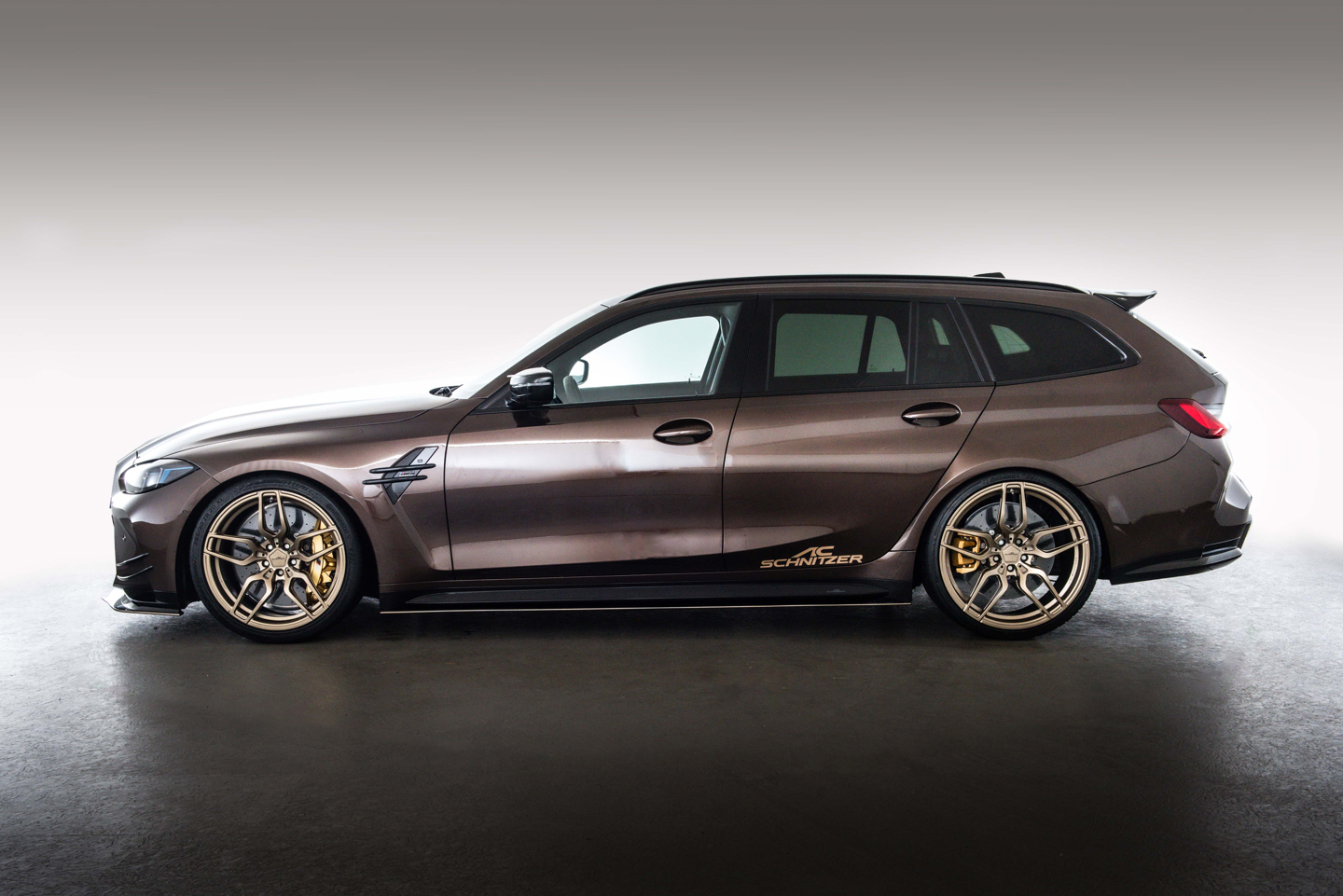 BMW M3 Touring in Braun mit AC Schnitzer Tuningpaket, darunter goldene Leichtmetallräder, sportliche Seitenschweller, Frontsplitter und dezentem Schriftzug an der Seite. Das Fahrzeug ist seitlich im Studio vor hellem Hintergrund fotografiert.