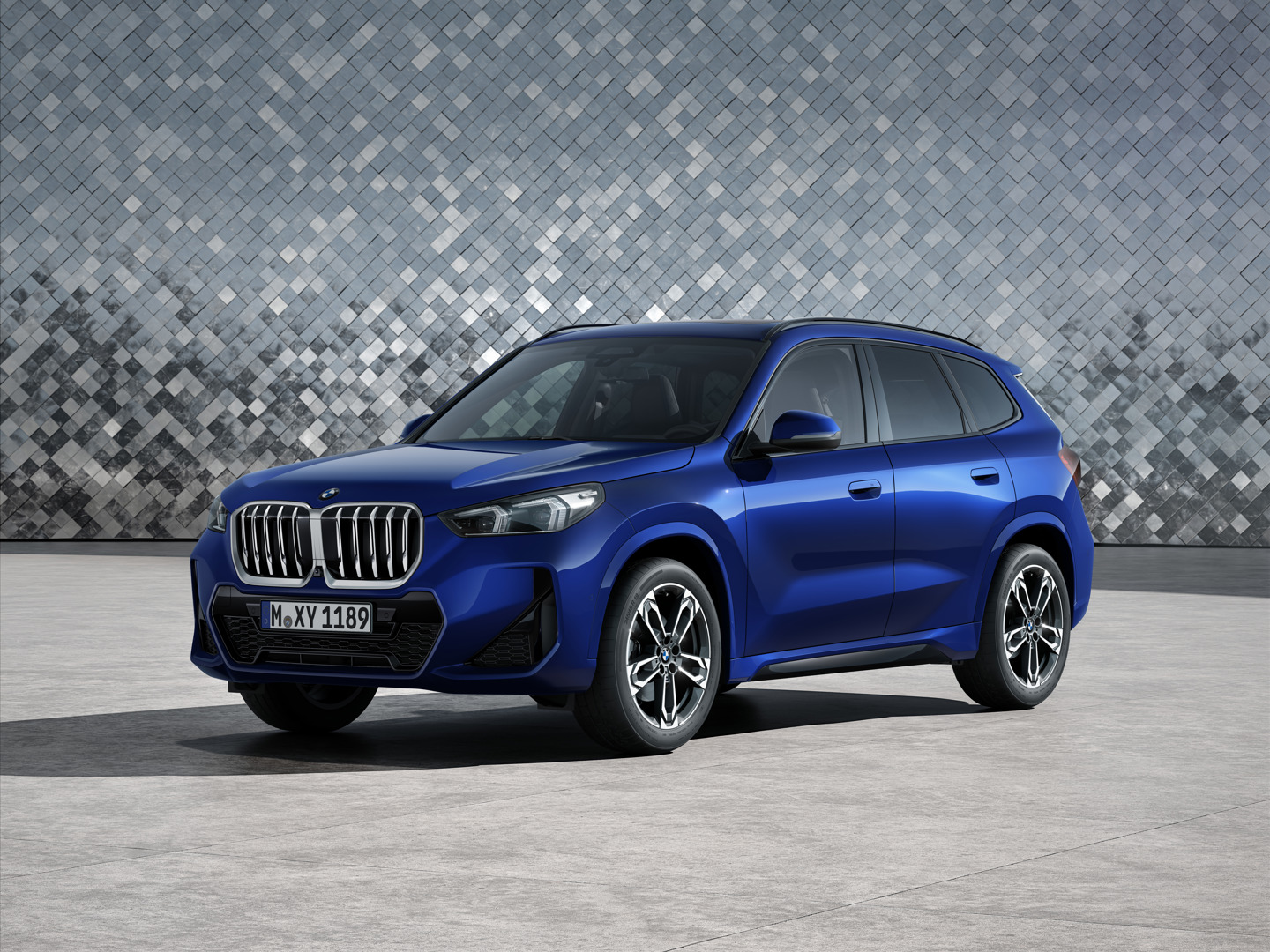 Ein blauer BMW-SUV, der auf einer Betonfläche vor einer grauen, gefliesten Wand geparkt ist.